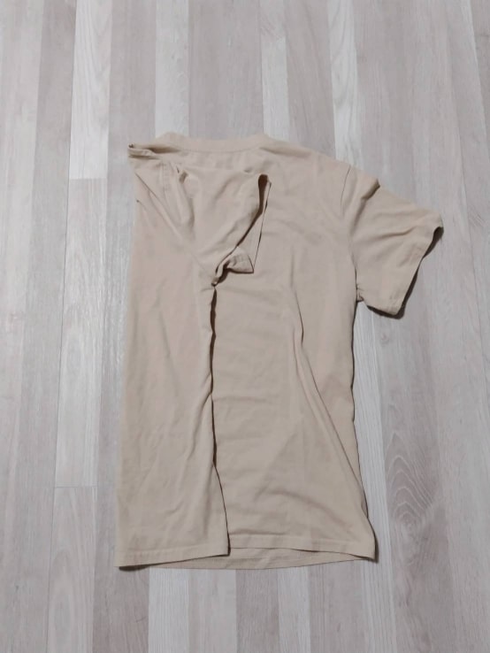 Tシャツを後ろ向きにして広げ、片方の袖を折りたたみます